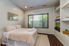 a bed sitting in a bedroom next to a window covered in white sheets and pillows