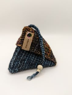 a blue and brown knitted bag with a tag attached to the front, sitting on a white surface