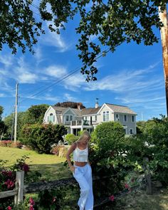 a woman in white pants and crop top standing on the side of a road next to a house