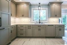 a kitchen with gray cabinets and white counter tops, along with a window over the sink