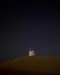 a man sitting on top of a sand dune under a night sky filled with stars