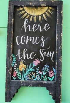 there is a chalkboard sign with the words here comes the sun written on it