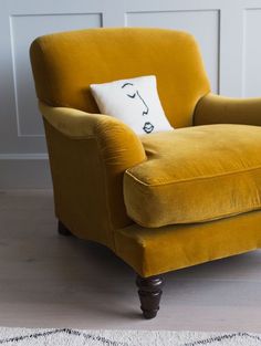 a yellow chair sitting on top of a wooden floor next to a white rug and wall