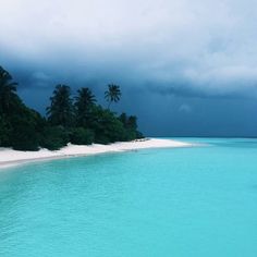 the water is very blue and clear with palm trees in the background on an overcast day