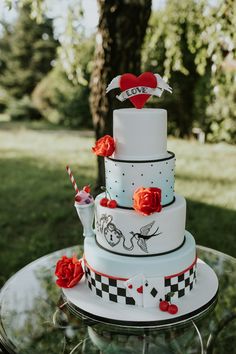 a three tiered cake with red roses on top sitting on a glass table outside