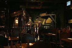 an old fashioned bar with wooden tables and chairs in the dark, filled with liquor bottles