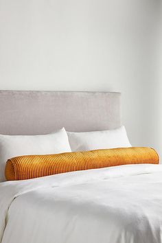 a bed with white linens and orange striped pillows on top of it's headboard