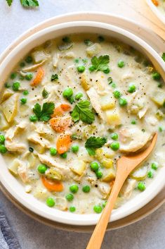 a white bowl filled with chicken and vegetable soup next to a wooden spoon on top of a table