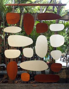 a group of different shapes and sizes of mirrors hanging from a ceiling in front of palm trees