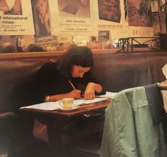 a woman sitting at a table writing on a piece of paper with a cup of coffee in front of her