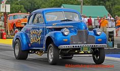 an old blue truck driving down a race track