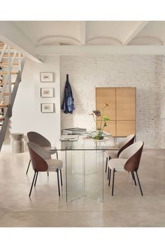 a glass table with chairs around it in front of a stair case and wooden cabinet