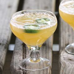 two glasses filled with yellow liquid and cucumber garnish on wooden table