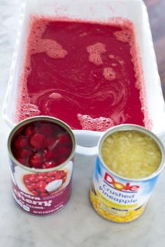 three cans of food sitting on top of a table next to two cups with liquid in them