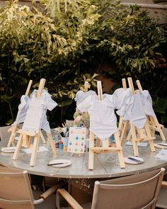 an outdoor table set up with clothes on wooden easels and other items sitting on chairs