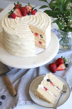 there is a cake with white frosting and strawberries on the plate next to it