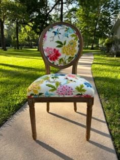 a chair sitting on top of a sidewalk next to a lush green field with trees