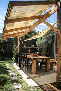 Outdoor patio with wooden pergola and retractable shades. Furnished with a wooden table, black chairs, and surrounded by plants. Stone pathway leads to the patio. Diy Backyard Shade Ideas, Diy Backyard Shade, Shade For Backyard, Backyard Shade Ideas, Resort House, Backyard Shade, Shade Ideas, Backyard Gardens, Diy Shades