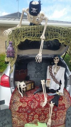 two skeletons sitting in the trunk of a car decorated with grass and fake skeleton decorations