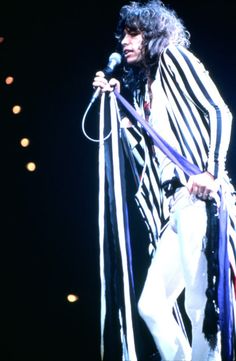 an image of a man that is on stage holding a microphone and wearing white pants