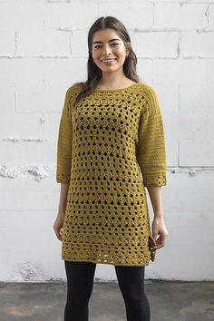 a woman standing in front of a white brick wall wearing a yellow sweater and black leggings