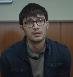 a man with glasses sitting down in front of a desk and looking at the camera