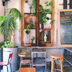 an outdoor cafe with potted plants on the wall and two wooden stools in front