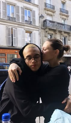 a man and woman hugging each other in front of a building