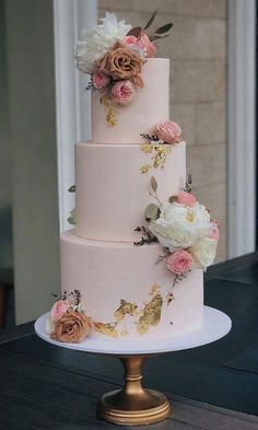 a three tiered wedding cake with pink and white flowers on the top, sitting on a gold pedestal