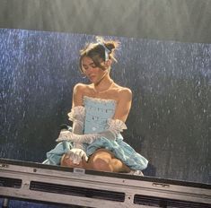 a woman in a blue dress sitting on top of a tv screen with rain coming down