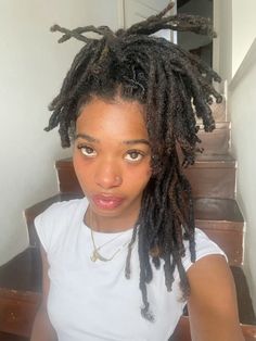 a woman with dreadlocks on her head is sitting in front of stairs and looking at the camera