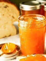 an orange jam in a jar next to sliced bread