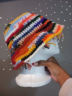 a hand is holding onto a multicolored hat on a mannequin head