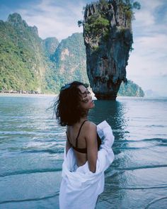 a woman standing in the water looking up at an island