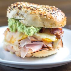 a sandwich with meat, cheese and guacamole on a white plate sitting on a wooden table