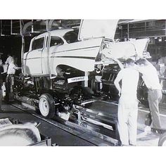 an old black and white photo of men working on a truck in a factory with people standing around