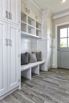 a room with some white cabinets and gray pillows on the bench in front of it