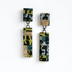 two square shaped earrings hanging from chains on a white surface with black and green designs