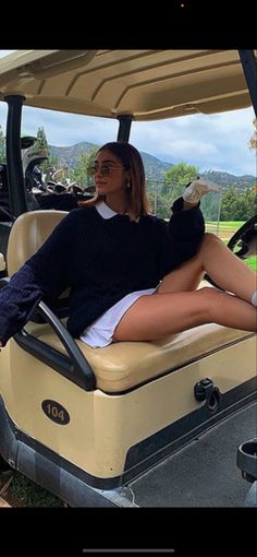 a woman sitting in the back of a golf cart with her legs crossed on the ground