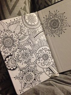 an open notebook sitting on top of a bed next to a drawing book with intricate designs