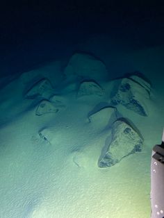 an underwater view of some rocks and snow in the water with a light shining on them