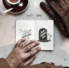 a person's hand on top of an open book next to a cup of coffee