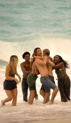 a group of people standing on top of a sandy beach next to the ocean with one person hugging another