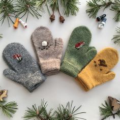 four knit mittens sitting on top of a white surface next to pine needles and cones