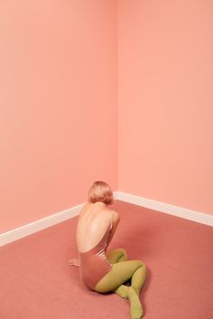 a woman sitting on the floor in a room with pink walls and green tights