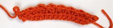 an orange crochet piece on a white surface