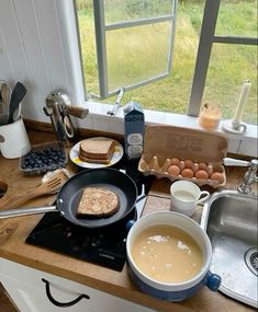 the kitchen counter is cluttered with food and utensils, including bread, eggs, milk, butter, and water