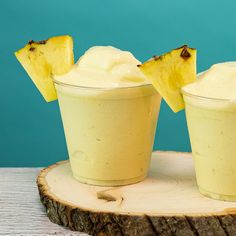 two glasses filled with ice cream and pineapple slices on top of a wooden slice