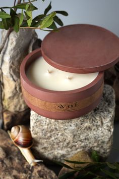 a candle in a round box sitting on top of a rock next to a snail