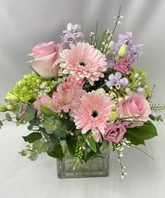 a vase filled with pink and purple flowers on top of a white table next to greenery